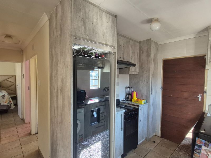 A functional kitchen featuring modern wood-look cabinetry, a freestanding stove with extractor fan, and tiled flooring, with direct access to the hallway.