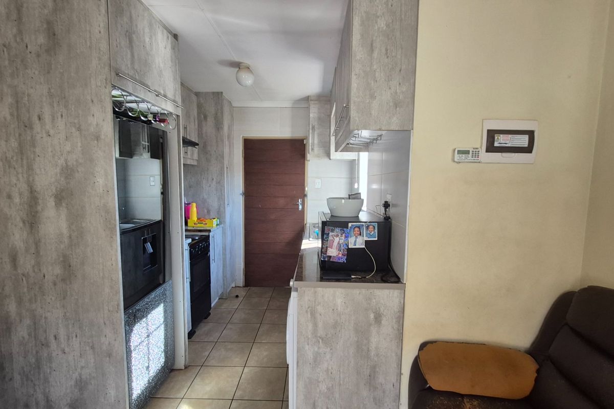 A functional kitchen featuring modern grey-toned cabinetry, tiled flooring, and integrated cooking appliances, providing a practical workspace with direct access to the home.