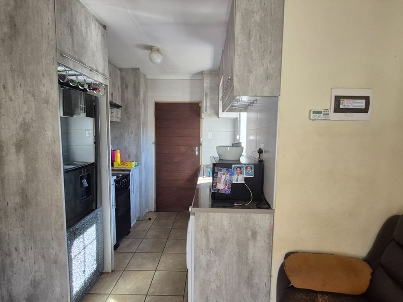 A functional kitchen featuring modern grey-toned cabinetry, tiled flooring, and integrated cooking appliances, providing a practical workspace with direct access to the home.