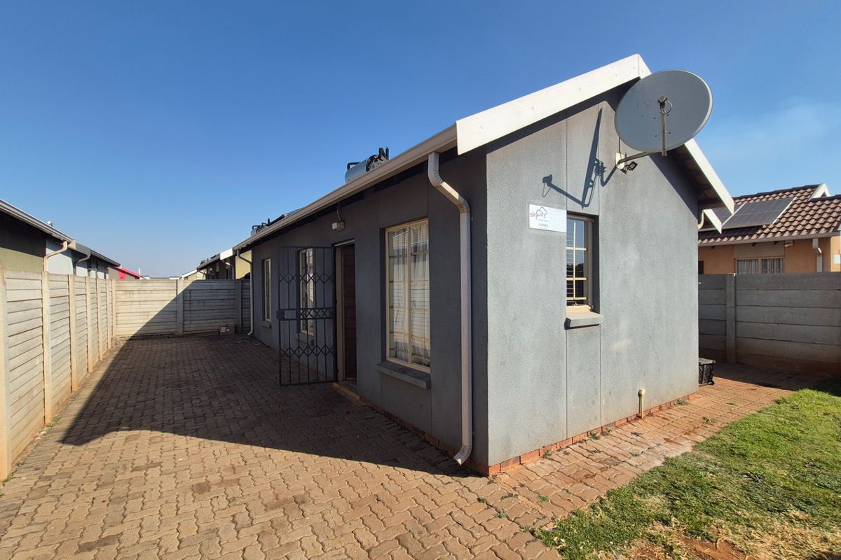 Rear view of the property featuring a paved courtyard, precast boundary walls, and a secure entrance with a metal security gate.