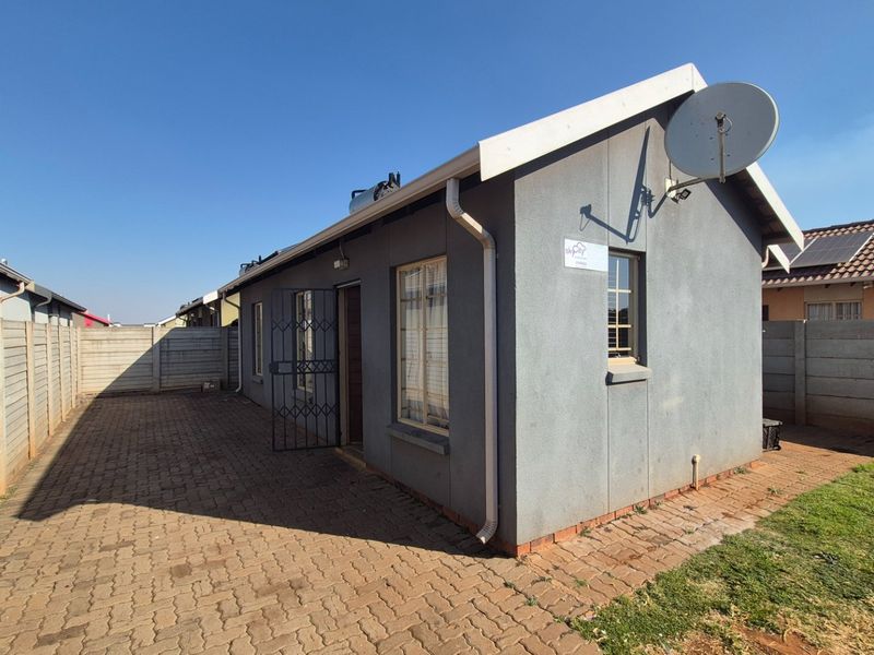 Rear view of the property featuring a paved courtyard, precast boundary walls, and a secure entrance with a metal security gate.