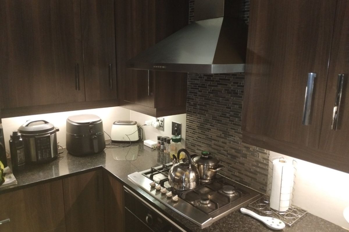 A modern kitchen featuring dark wood cabinetry, granite countertops, a gas hob with stainless steel extractor fan, and a decorative mosaic tile backsplash.