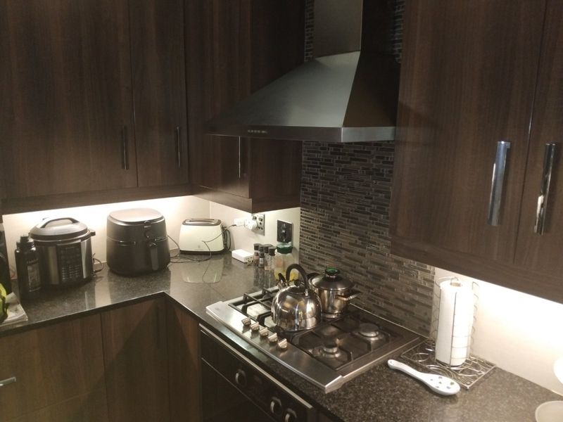 A modern kitchen featuring dark wood cabinetry, granite countertops, a gas hob with stainless steel extractor fan, and a decorative mosaic tile backsplash.