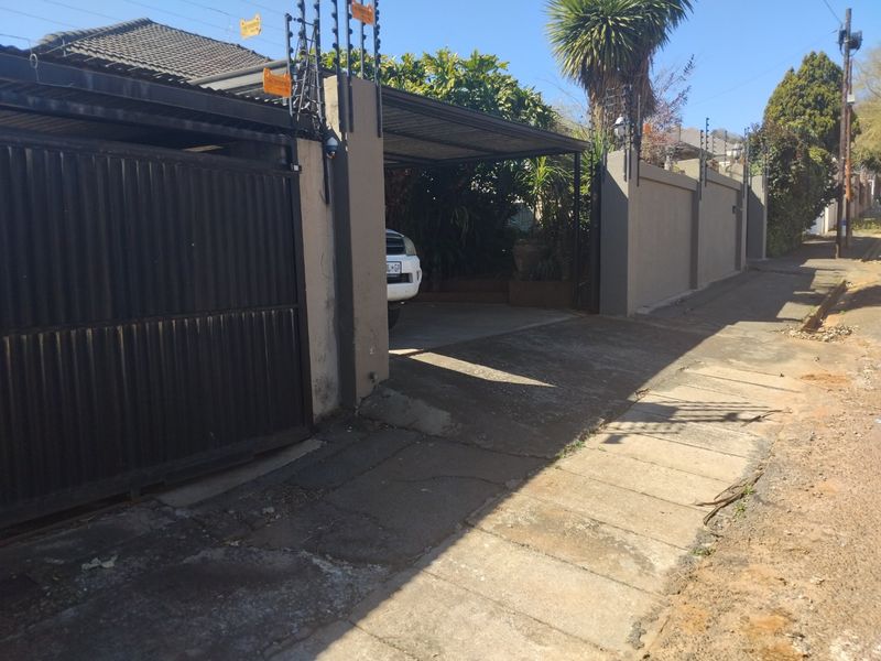 Front exterior view showing a gated entrance, carport, and perimeter wall with electric fencing along the street boundary.