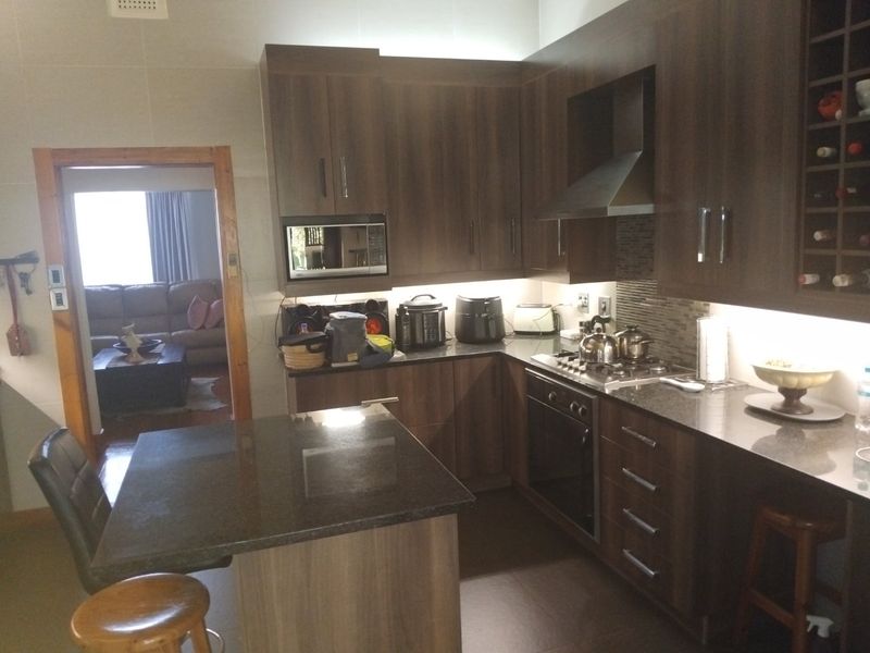 Modern kitchen featuring dark wood cabinetry, granite countertops, a central island, and integrated appliances including a gas hob and oven.