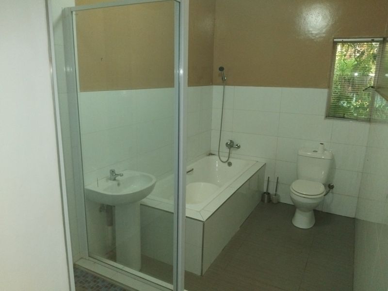 A functional bathroom featuring a pedestal basin, built-in bathtub, separate shower enclosure, and toilet with neutral wall tiling.