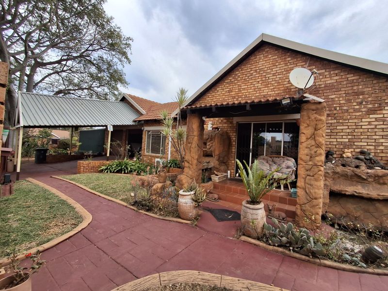 Front view of a face brick house featuring a covered carport, paved walkway, and decorative stone pillars at the entrance.
