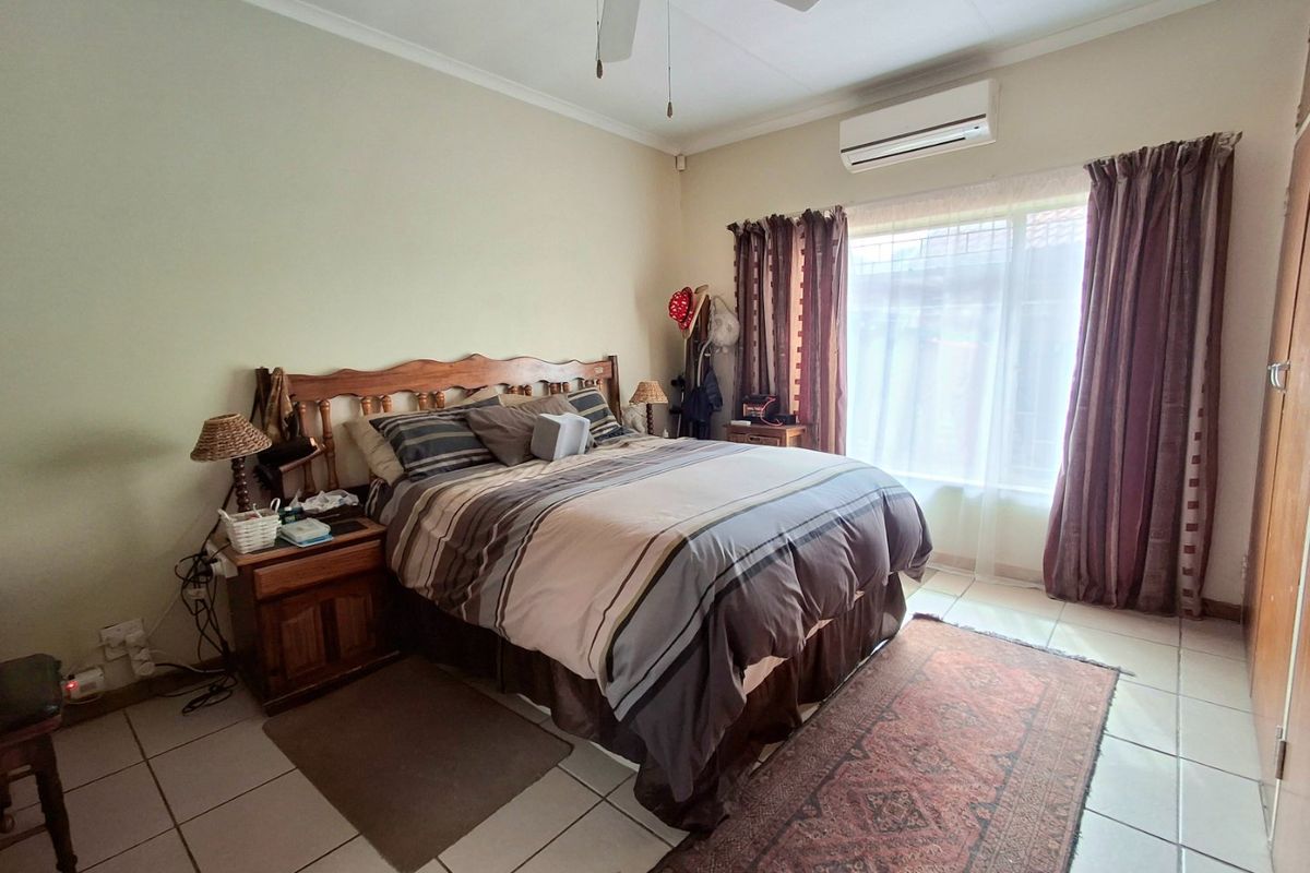 A functional bedroom featuring tiled flooring, a ceiling fan, and a wall-mounted split-system air conditioner for climate control.