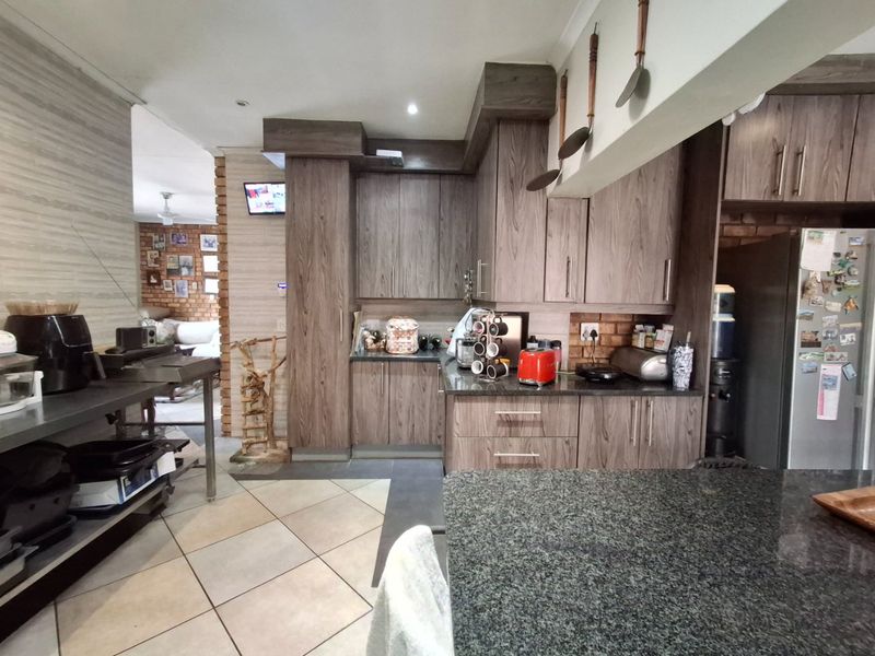 A functional kitchen featuring wood-grain cabinetry, granite countertops, and tiled flooring, with an open-plan layout connecting to the adjacent living area.