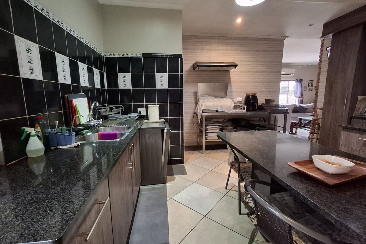 A functional kitchen featuring granite countertops, a double sink, tiled backsplash, and built-in cabinetry, with an open-plan layout leading to the living area.
