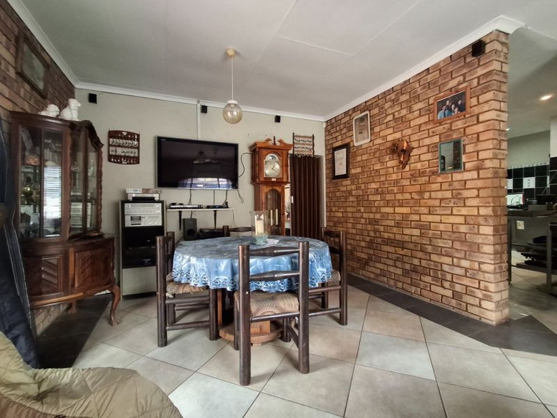 Open-plan living and dining area featuring a prominent exposed brick wall and neutral ceramic floor tiling.