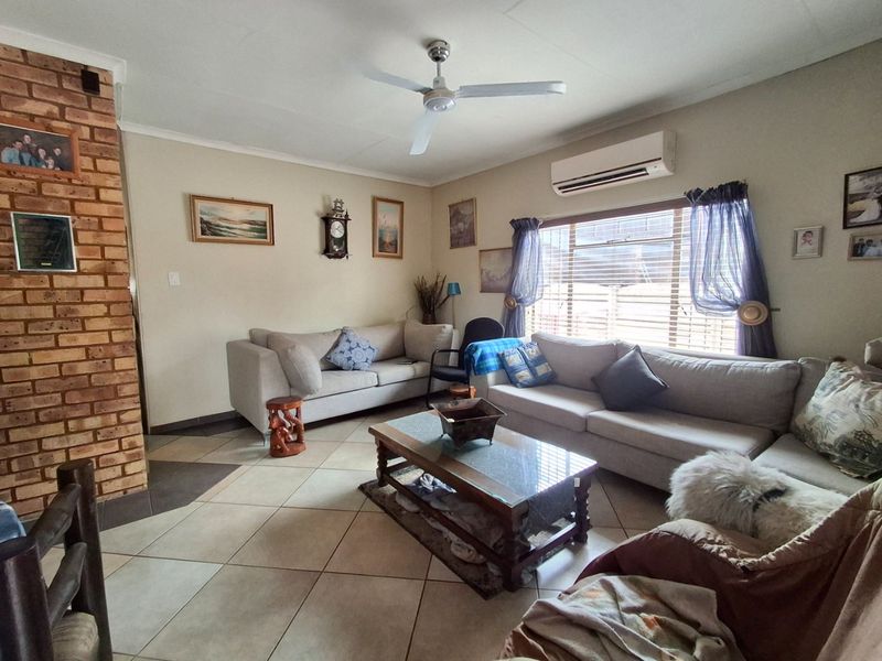 A comfortable living room featuring tiled flooring, an exposed brick fireplace, a ceiling fan, and a wall-mounted split-system air conditioner.