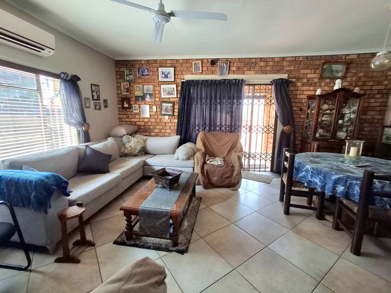 Open-plan living and dining area featuring exposed brick walls, ceramic floor tiles, a ceiling fan, and split-system air conditioning with access to the exterior.