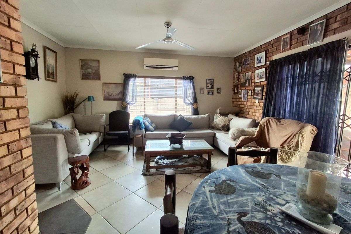 Spacious living room featuring an exposed brick wall, tiled flooring, ceiling fan, and a wall-mounted air conditioning unit.