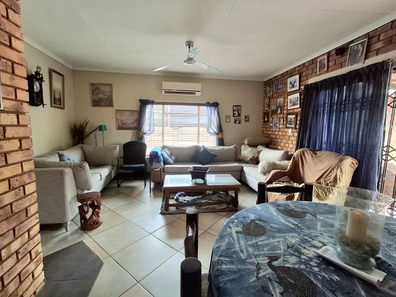 Spacious living room featuring an exposed brick wall, tiled flooring, ceiling fan, and a wall-mounted air conditioning unit.