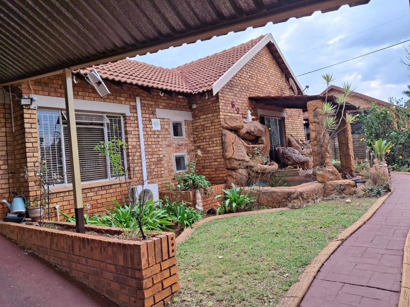 Front exterior view of a face brick house featuring a tiled roof, carport, paved walkway, and a decorative built-in rock water feature.