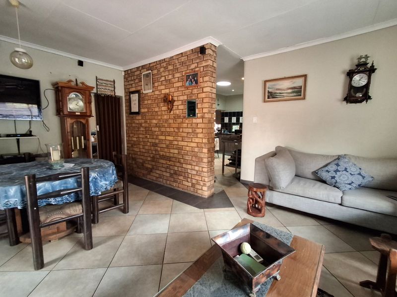 Open plan living and dining area featuring a prominent exposed brick partition wall and neutral ceramic floor tiling throughout.