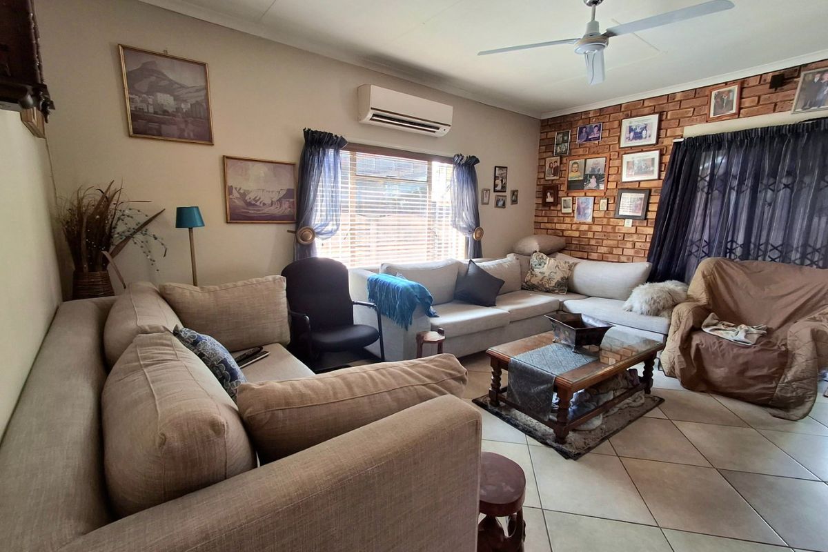 A comfortable living room featuring an exposed brick accent wall, tiled flooring, a ceiling fan, and a wall-mounted air conditioning unit.