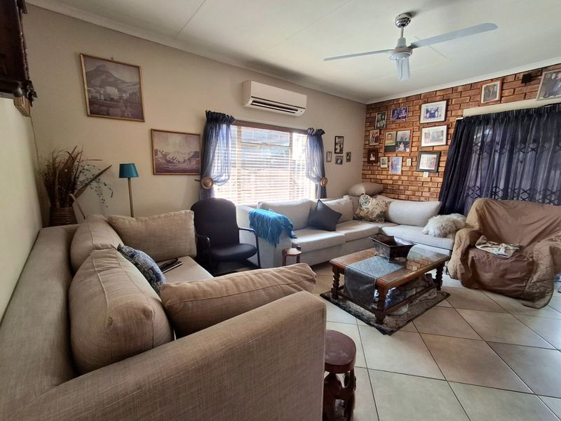 A comfortable living room featuring an exposed brick accent wall, tiled flooring, a ceiling fan, and a wall-mounted air conditioning unit.