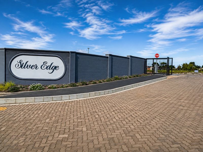 Entrance view of the Silver Edge estate featuring a paved driveway, secure gated access, and a prominent perimeter wall.