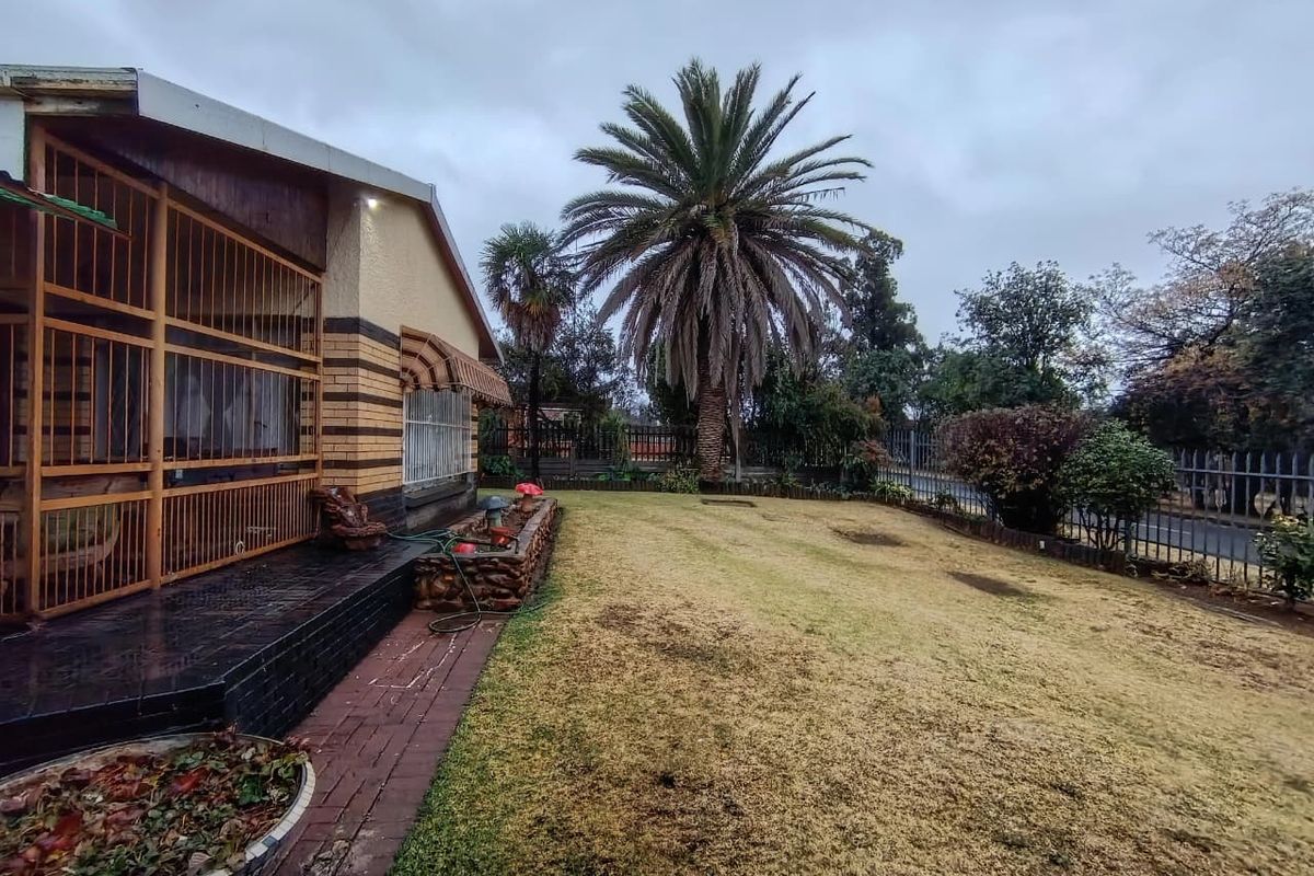 A rear garden view featuring a lawn, mature palm tree, and an enclosed patio area with brick paving and stone-clad planter.