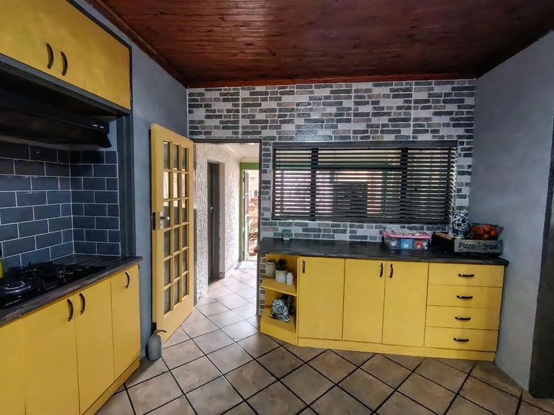 A kitchen featuring yellow cabinetry, a gas hob with extractor, tiled floors, and a distinctive exposed brick wall with timber ceiling finishes.