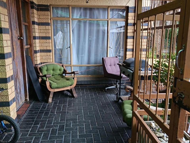 A covered patio area featuring dark brick paving, face brick walls, and a secure metal gate, providing a functional outdoor space.