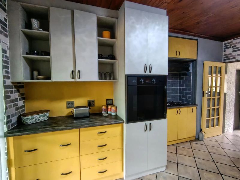 A functional kitchen featuring yellow cabinetry, built-in oven, hob, extractor fan, and tiled flooring with a contrasting backsplash.