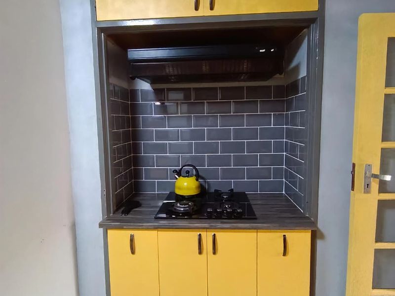 A compact kitchen nook featuring yellow cabinetry, a dark subway tile backsplash, and a built-in gas hob with an extractor fan.