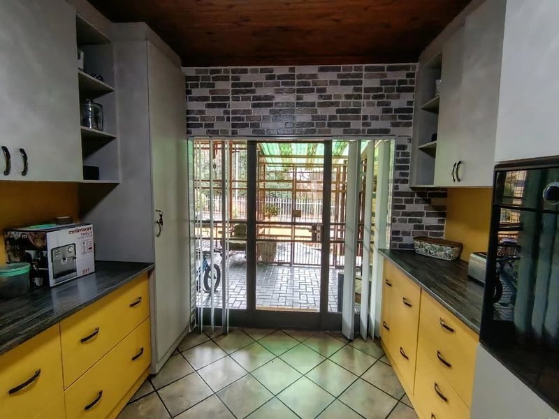 A galley-style kitchen featuring yellow cabinetry, dark countertops, a brick-effect feature wall, and direct access to an outdoor patio area.