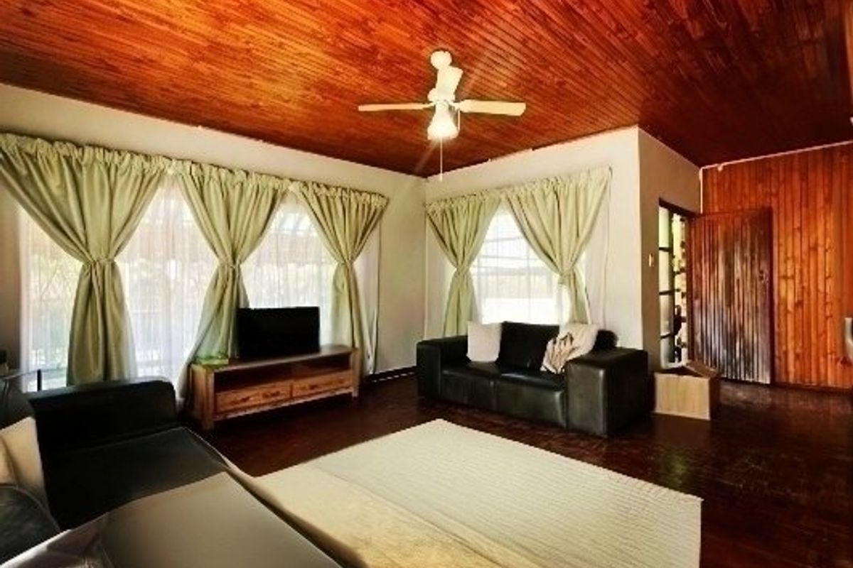 Spacious living room featuring warm timber ceiling and flooring, complemented by timber wall paneling and a central ceiling fan.
