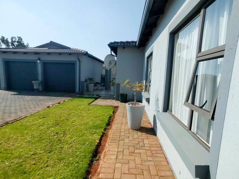 A well-maintained front exterior view featuring a paved driveway, double garage, and a neat walkway alongside the main house structure.