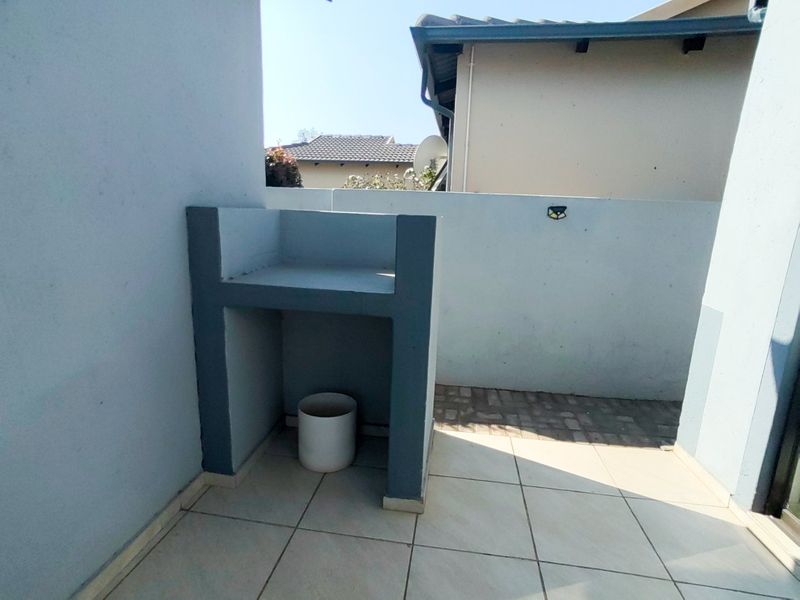 A covered patio area featuring a built-in braai, tiled flooring, and a private boundary wall, offering a functional outdoor entertainment space.