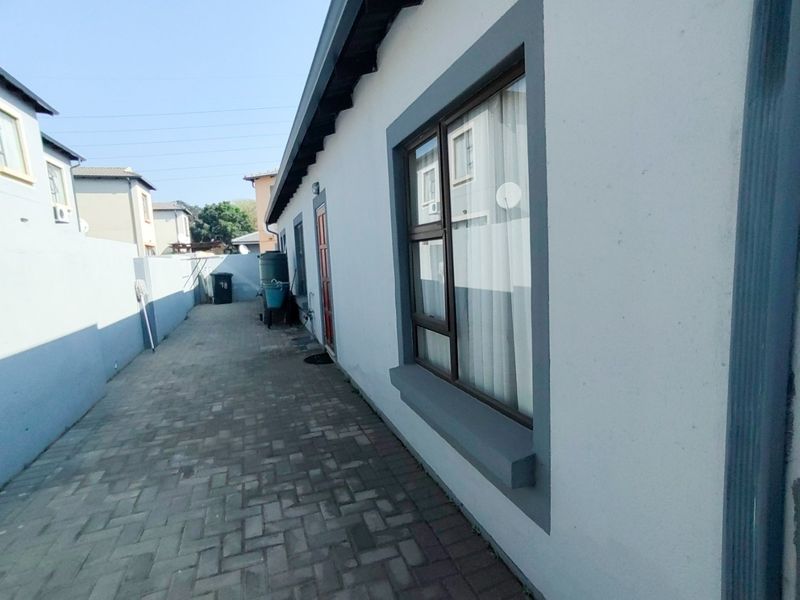 A side exterior view of the property featuring a paved walkway, boundary wall, and aluminium window frames along the side elevation.