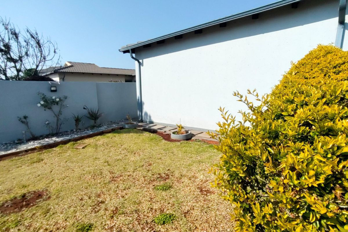 A view of the rear garden area featuring a boundary wall, paved walkway, and established landscaping along the side of the house.