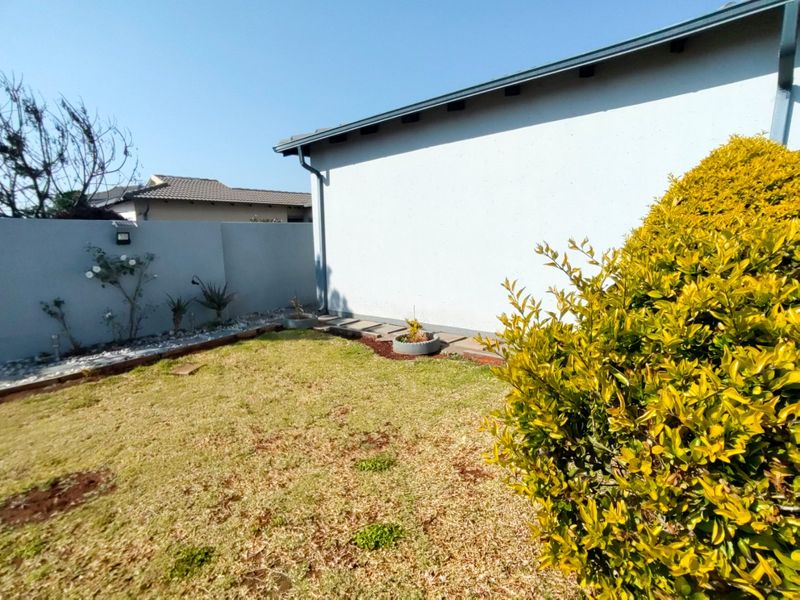 A view of the rear garden area featuring a boundary wall, paved walkway, and established landscaping along the side of the house.