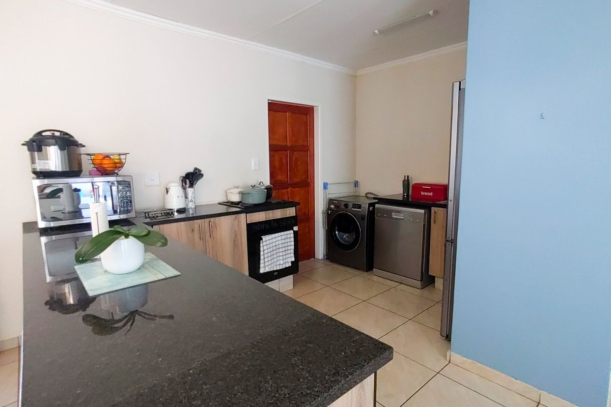 A functional kitchen featuring granite countertops, built-in cabinetry, a hob, and an oven, with tiled flooring and space for laundry appliances.