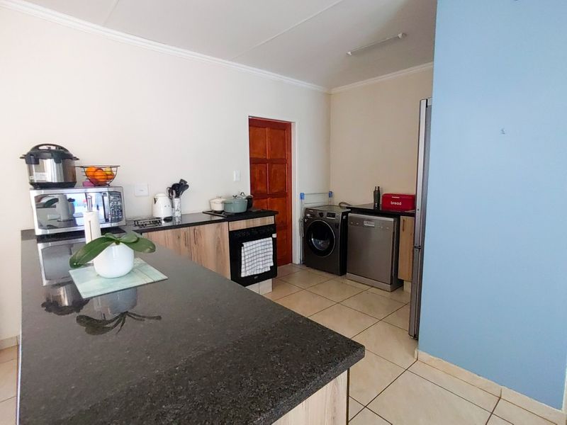 A functional kitchen featuring granite countertops, built-in cabinetry, a hob, and an oven, with tiled flooring and space for laundry appliances.