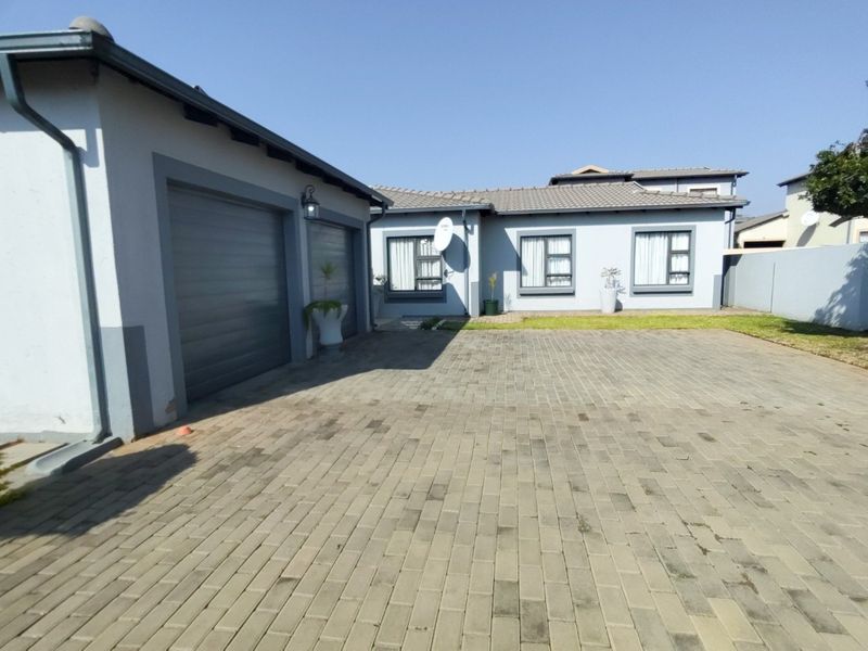 Front view of the property featuring a paved driveway, double garage, and well-maintained exterior facade with tiled roofing and aluminium window frames.