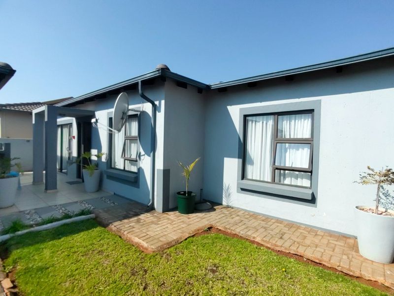 A well-maintained front exterior view of a modern house featuring grey painted walls, dark window frames, and a paved walkway leading to the entrance.