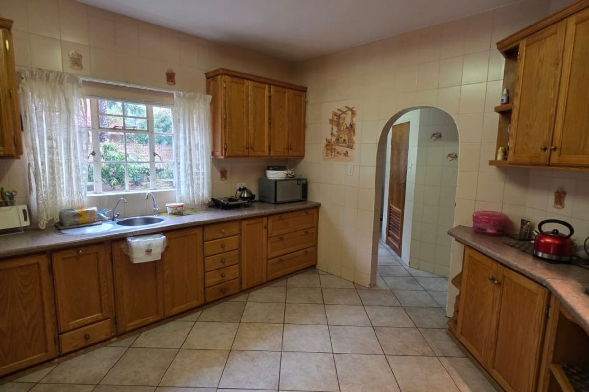 A functional kitchen featuring wooden cabinetry, laminate countertops, ceramic tiling, and an arched doorway leading to an adjacent utility area.