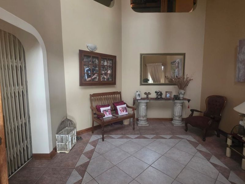 Spacious double-volume entrance hall featuring tiled flooring, decorative cut-outs overlooking the upper level, and a secure metal gate.