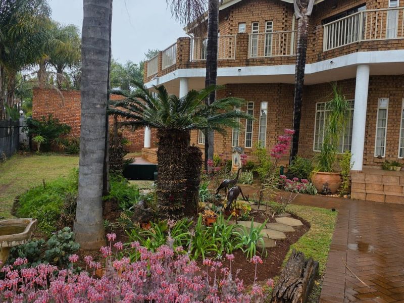 A view of the rear exterior of a double-story face brick house featuring a landscaped garden, paved walkway, and an upper-level balcony.