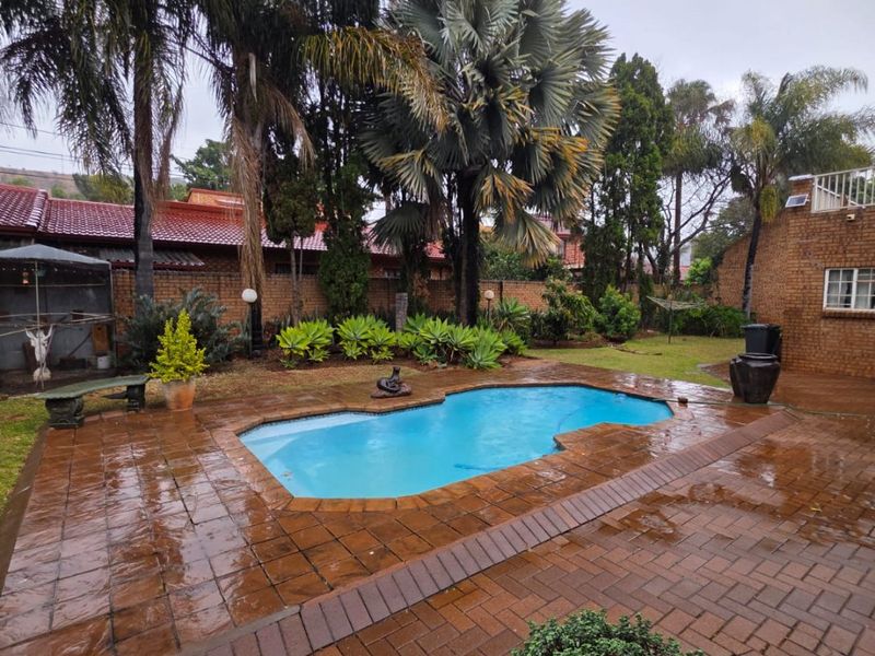 A private backyard featuring a swimming pool surrounded by brick paving and established garden landscaping.