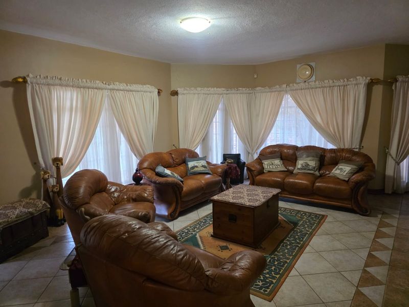 A spacious living room featuring tiled flooring, large windows with curtain rods, and a central ceiling light fixture.