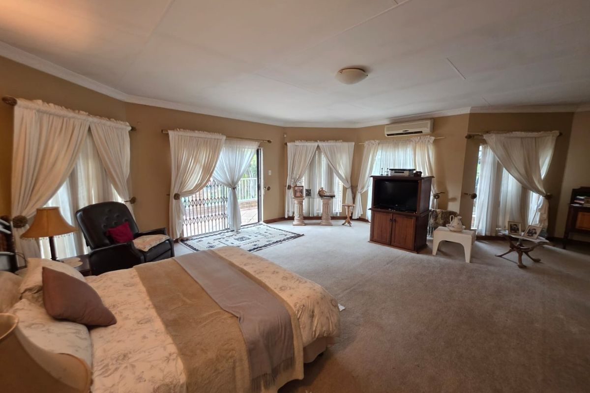 Spacious bedroom featuring carpeted flooring, coved ceilings, a wall-mounted air conditioning unit, and multiple sliding glass doors providing access to the exterior.