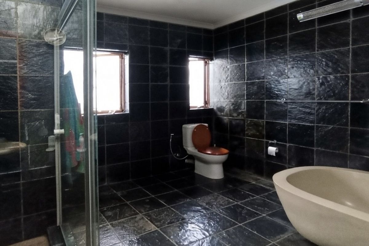 Spacious bathroom featuring dark slate wall and floor tiles, a freestanding bathtub, and a separate glass-enclosed shower area.