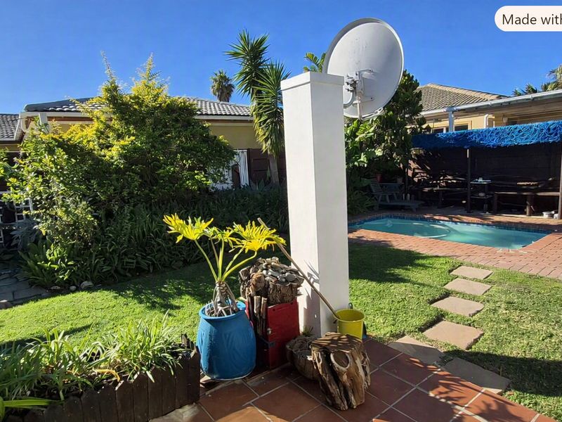 A backyard pool area featuring a swimming pool, brick paved patio, and established garden landscaping with a satellite dish mounted on a central pillar.