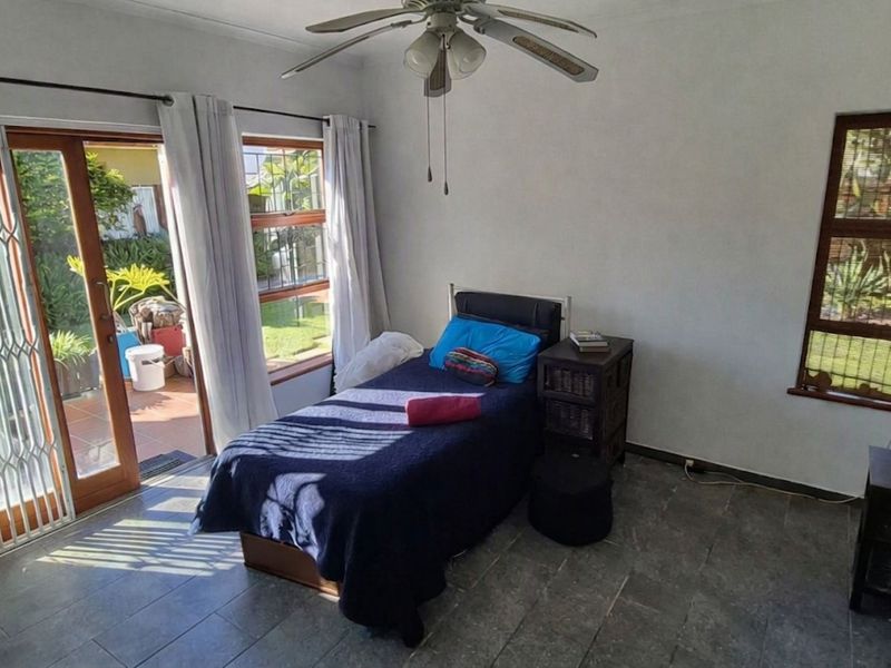 A bright bedroom featuring tiled flooring, a ceiling fan, and a sliding glass door providing direct access to the outdoor patio area.