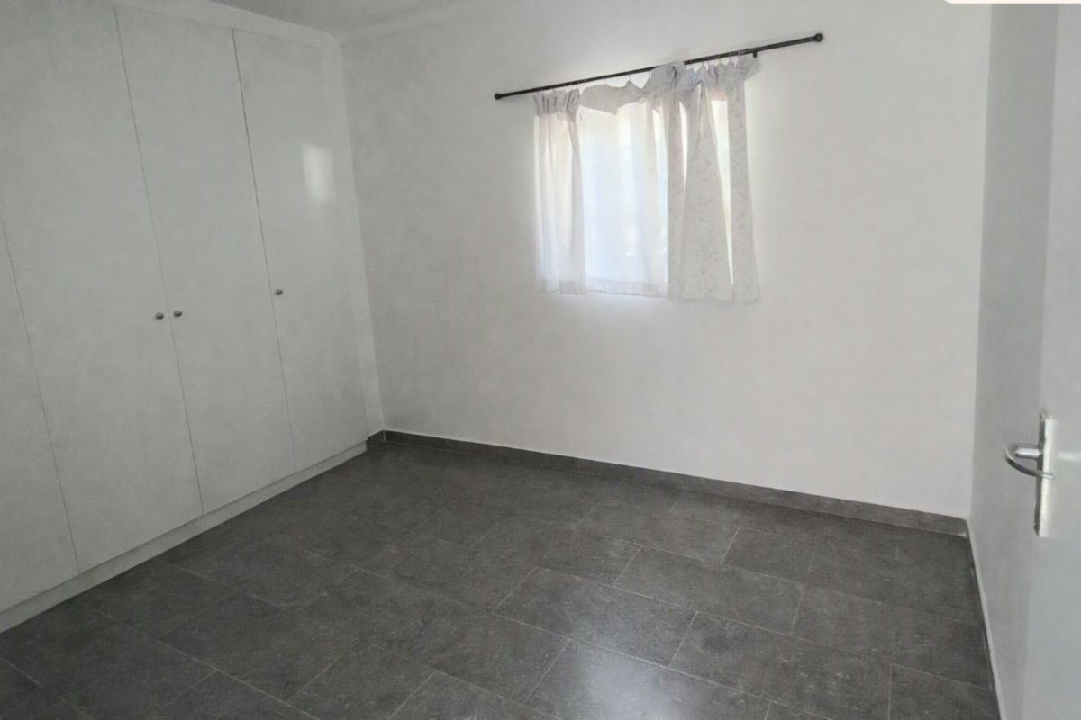 A clean, empty bedroom featuring neutral tiled flooring and built-in cupboards, offering a blank canvas for personalization.